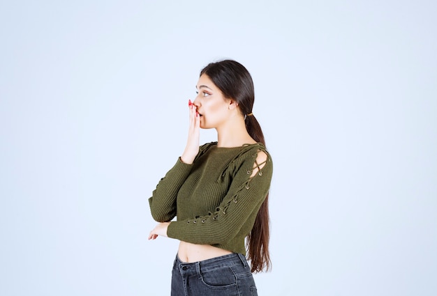 A shocked woman model standing and covering mouth with a hand.