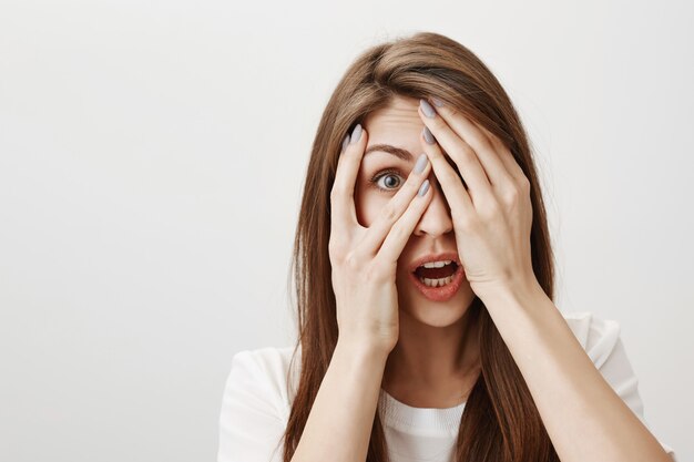 Shocked woman peeking through fingers with startled face
