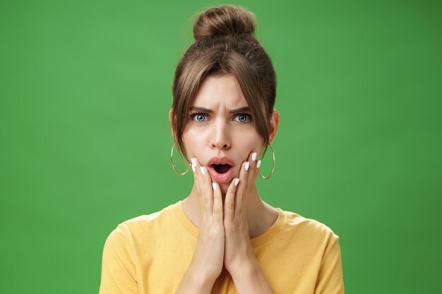 Shocked woman reacting to pimple looking disturbed and displeased in mirror holding hands pressed to...