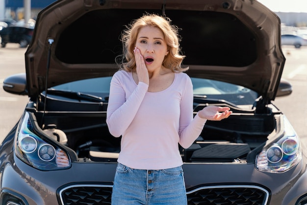 Shocked woman standing next to her broken car