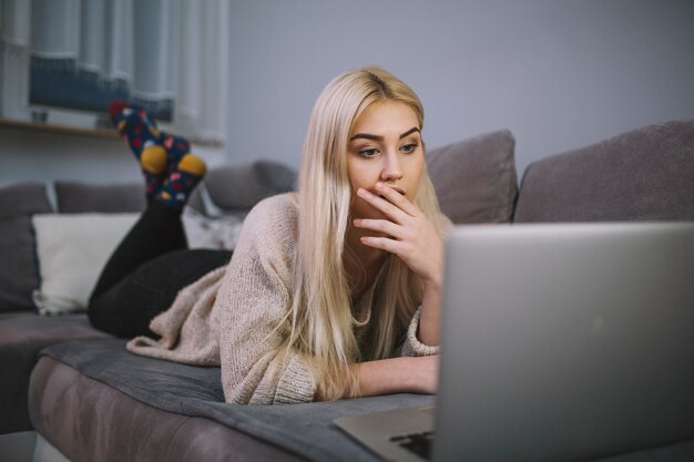 Shocked woman using laptop on sofa