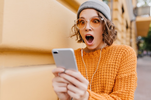 Shocked woman with brown eyes looking at phone screen with mouth open