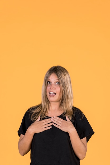 Shocked woman with mouth open standing in front of yellow wall