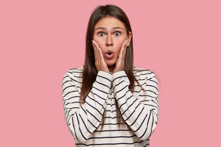 Free Photo shocked woman with terrified expression, keeps both hands on cheeks, gasps from wonder