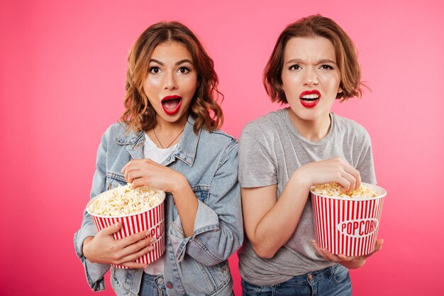 Shocked women friends eating popcorn watch film.