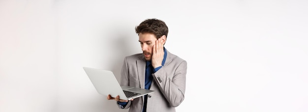 Uomo d'affari scioccato e preoccupato che fa errore sul laptop guardando il computer sconvolto in piedi sul bianco