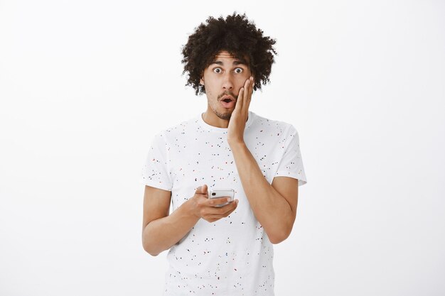 Shocked worried man react to something in his phone, looking startled, holding smartphone