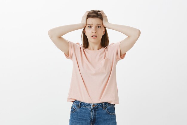 Shocked and worried woman have big problem, holding hands on head in denial