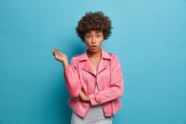 Shocked worried young Afro American woman has surprised embarrassed expression, keeps eyes widely opened, being well dressed, concerned about something, expresses great disbelief, stands indoor