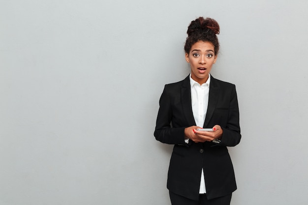 Shocked young african business woman standing over grey wall