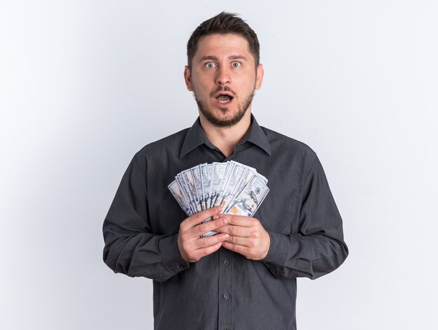 Shocked young blonde handsome man holding money with open mouth looking at camera 