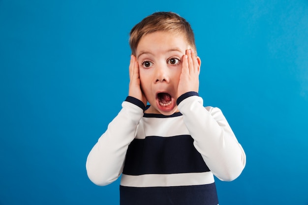 Free photo shocked young boy in sweater holding head and looking away