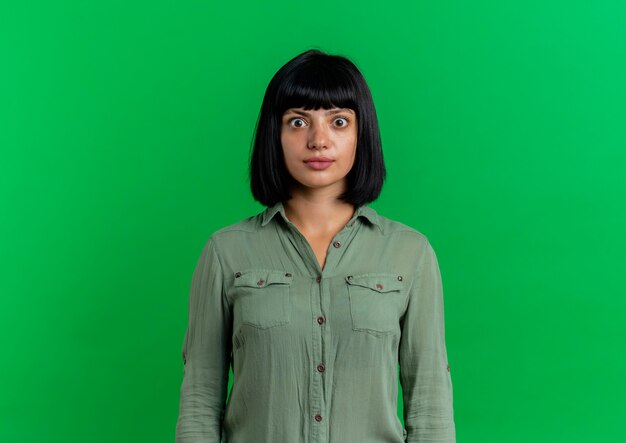 Shocked young brunette caucasian girl looks at camera isolated on green background with copy space