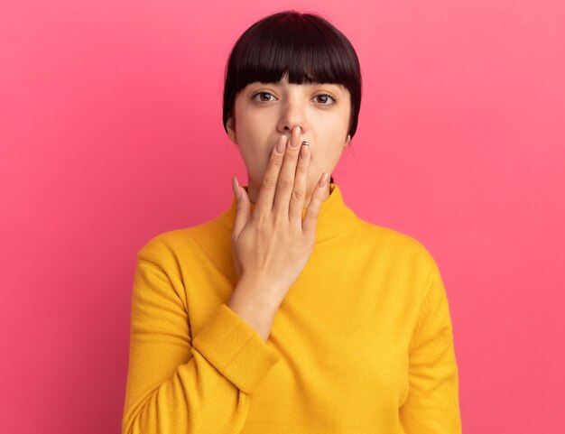 Shocked young brunette caucasian girl puts hand on mouth