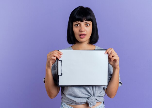 Free photo shocked young brunette caucasian woman holds clipboard