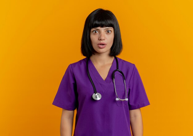 Shocked young brunette female doctor in uniform with stethoscope looks