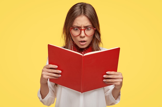 shocked young brunette with glasses posing against the yellow wall