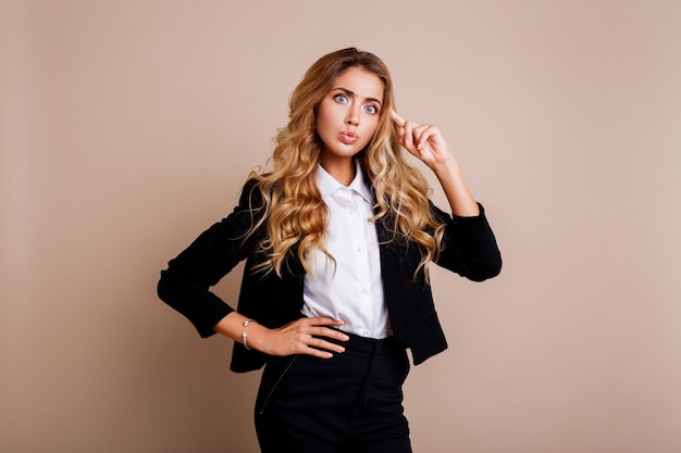 Shocked young business woman or employe in stylish suit posing over beige wall.