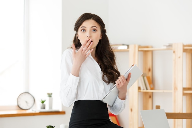 Free photo shocked young business woman surprised by reading unexpected news in document amazed woman office worker feeling stunned baffled by unbelievable information in paper about debt or dismissal