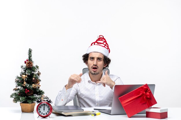 面白いサンタクロースの帽子と白い背景の上のオフィスでクリスマスを祝ってショックを受けた青年実業家