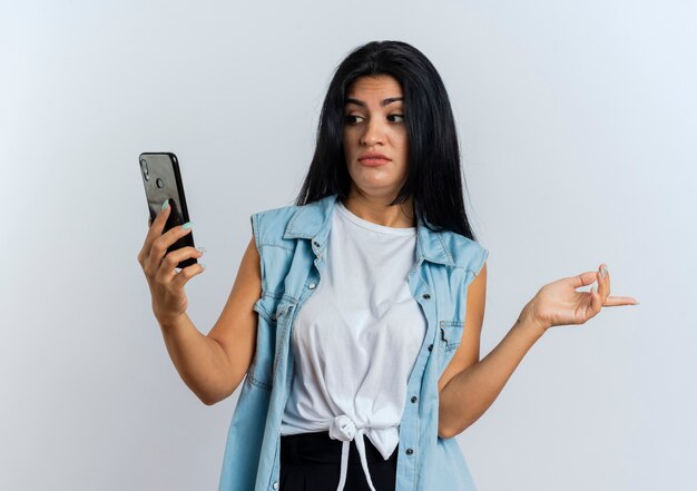 Shocked young caucasian woman looks at phone and points at side