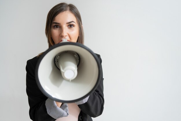 Shocked young Caucasian woman shouting at you in megaphone