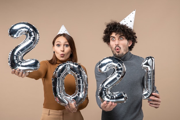 Shocked young couple wear new year hat poses for camera Girl showing and and guy with and on gray