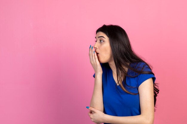 Shocked young girl closed her mouth with hand and looking aside on pink background High quality photo