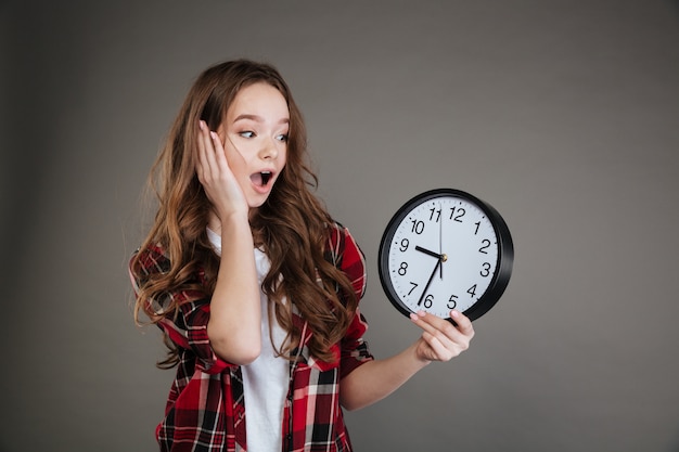 Foto gratuita orologio scioccato della tenuta della giovane signora. guardando da parte.