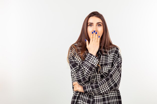 Shocked young lady holding her hand to her mouth and standing on white background