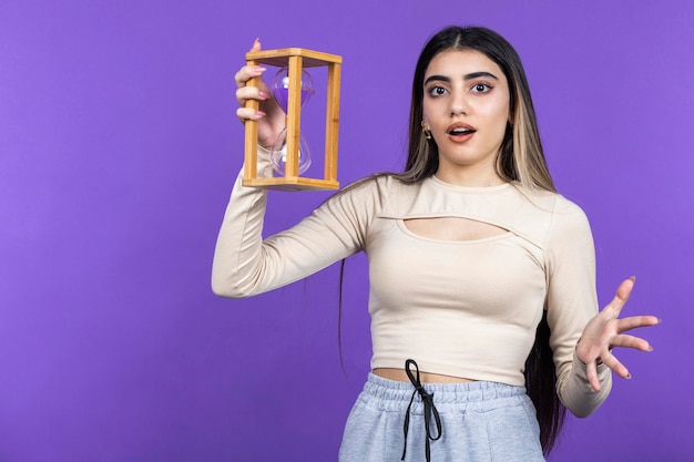 Free photo shocked young lady holding hour glass and looking at the camera high quality photo