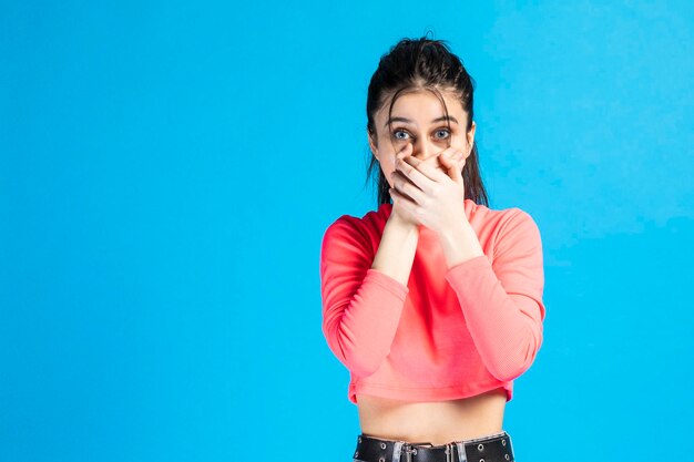 Shocked young lady put her hands to her mouth and look at the camera