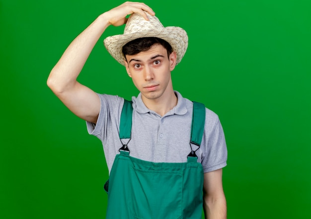 Foto gratuita giovane giardiniere maschio scioccato che indossa e che tiene il cappello di giardinaggio