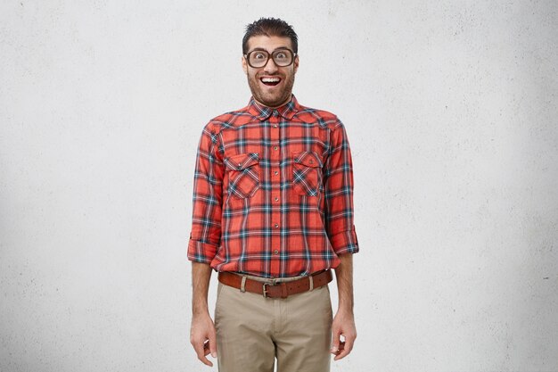 충격을받은 젊은 남성 괴상한은 오래된 유행 안경, 체크 무늬 셔츠 및 바지를 착용합니다.