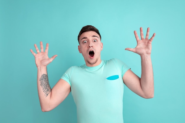 Shocked young man on blue studio wall