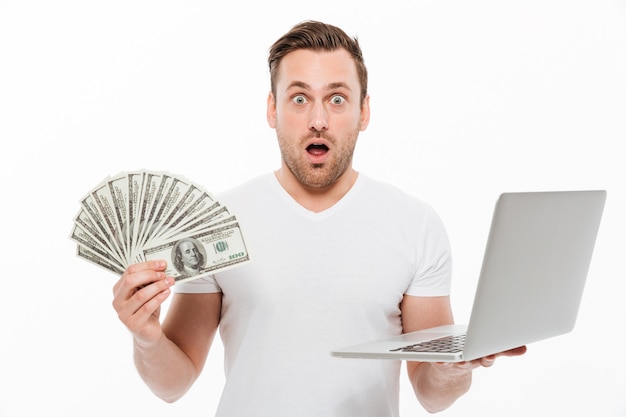 Shocked young man holding money using laptop computer.