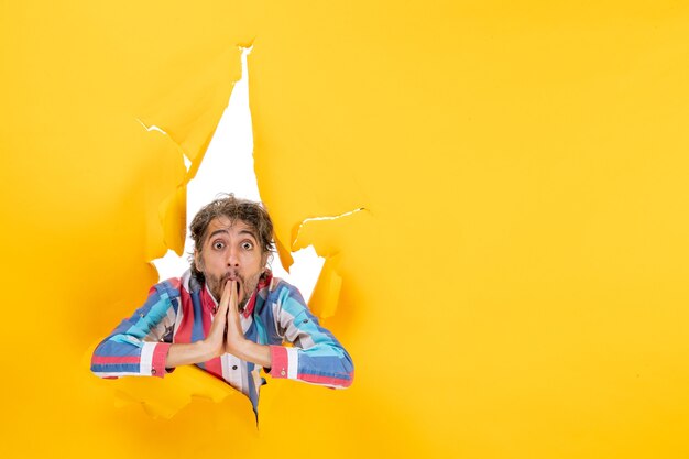 Shocked young man poses in torn yellow paper hole background