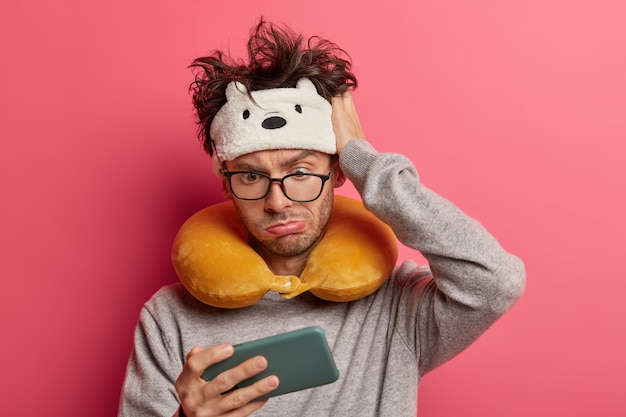 Shocked young man with messy hair stares at smartphone