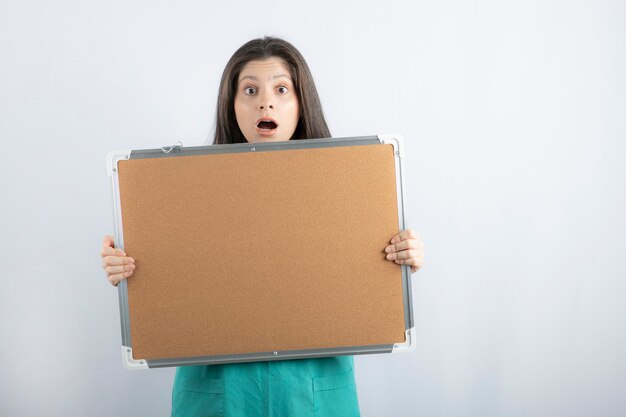 Shocked young nurse holding board with hand.