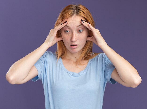 Shocked young redhead ginger girl with freckles puts hands on forehead and looks down