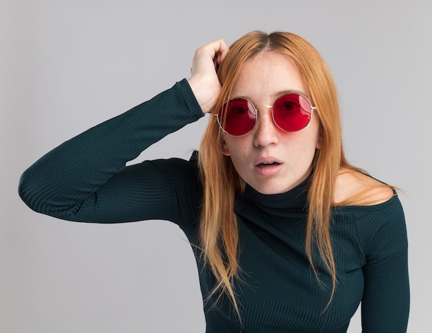 Shocked young redhead ginger girl with freckles in sun glasses puts hand on head isolated on white wall with copy space