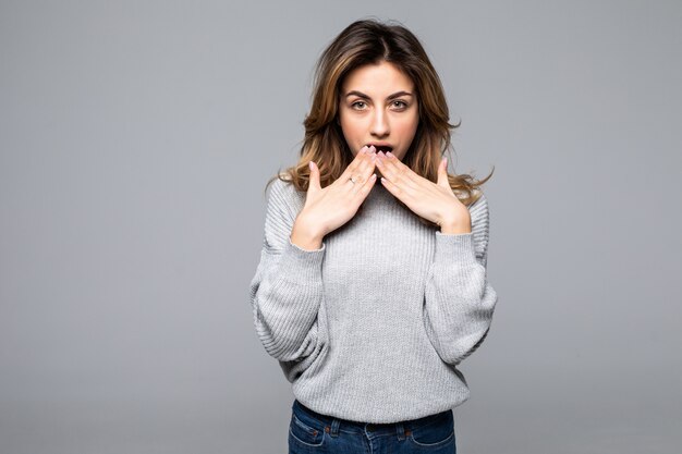 Shocked young woman in gray sweater put hands on cheeks isolated on grey wall.