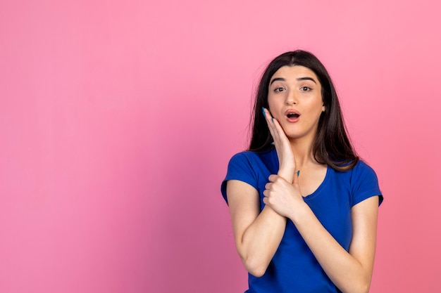 Giovane donna scioccata che tiene la mano sul viso e guarda la bocca aperta della fotocamera foto di alta qualità