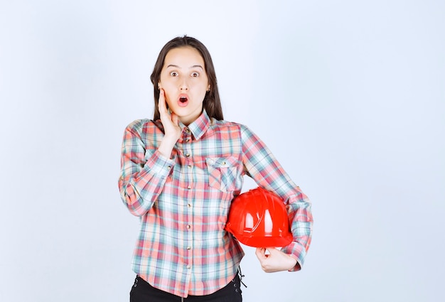 Shocked young woman holding red helmet on white background. 