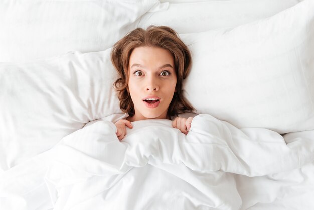 Shocked young woman lies in bed at morning