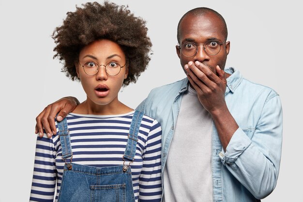 Shocked young woman and man open mouthes widely in bewilderment, embrace