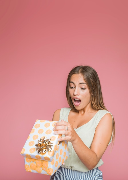 Shocked young woman opening floral gift box against pink background