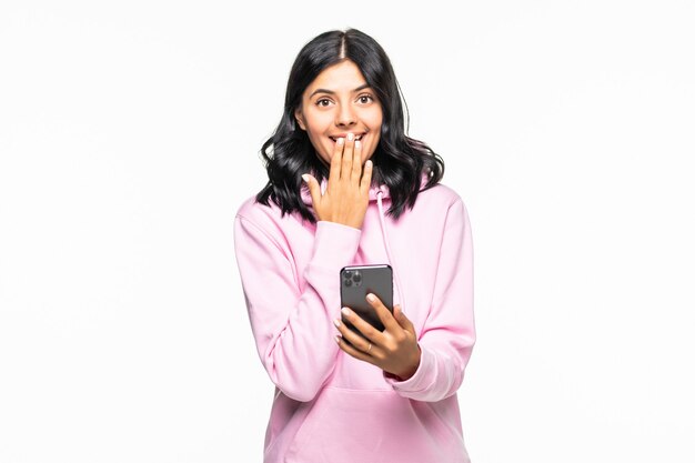 Shocked young woman Using mobile phone, typing sms message in casual hoodie posing isolated on grey wall wall