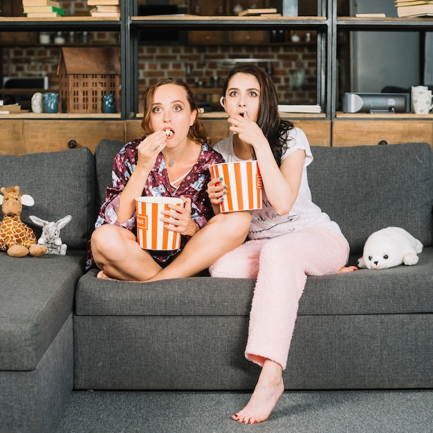 Free photo shocked young women sitting on sofa watching television