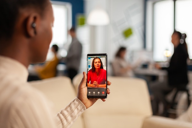 Foto gratuita sullo sholder del dipendente nero che discute con il partner in videochiamata utilizzando il telefono nell'ufficio di avvio